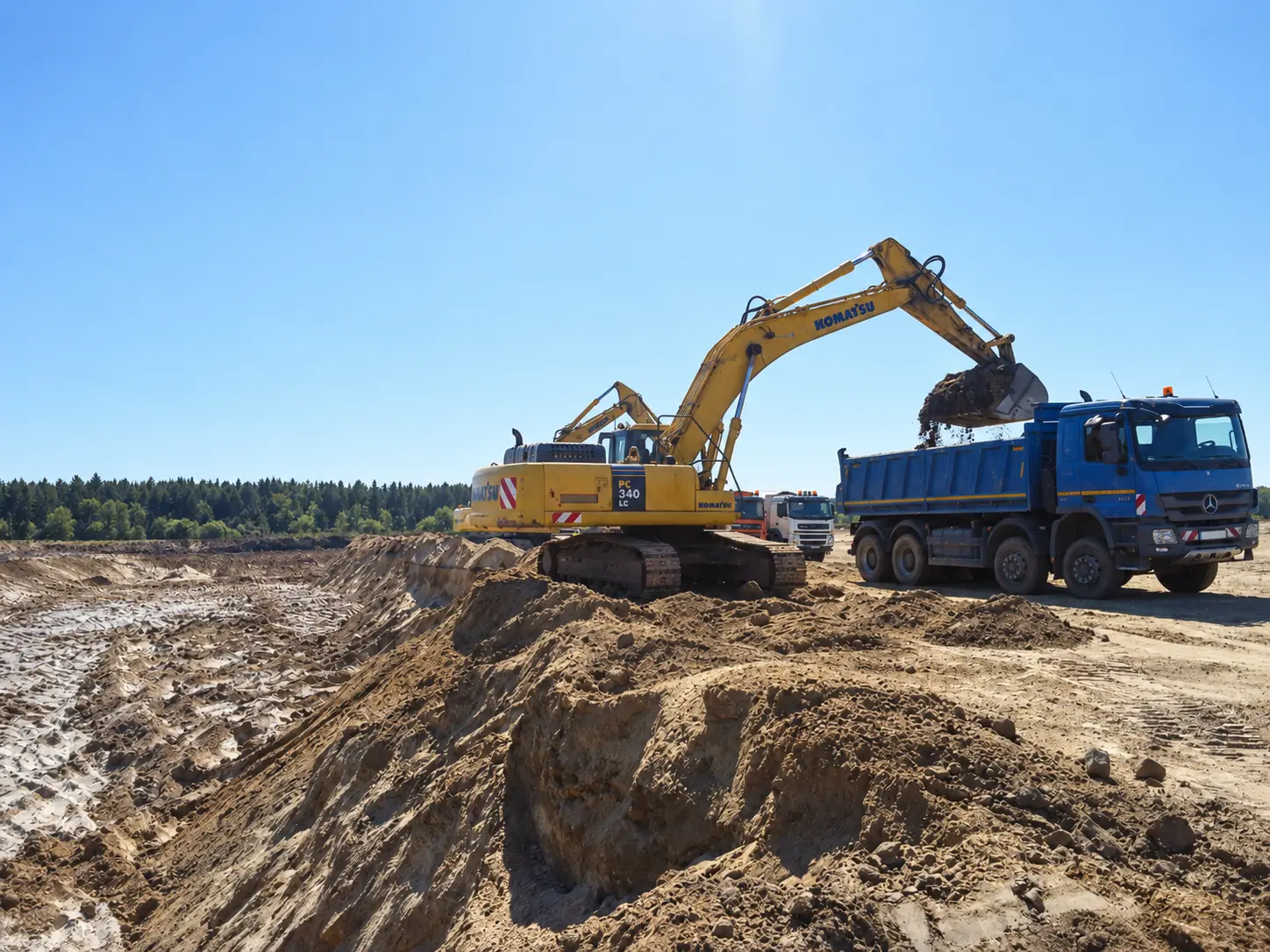Koparka Komatsu ładująca urobek na czteroosiową wywrotkę podczas robót ziemnych